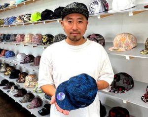 伝統織物を現代のキャップへ再生したワンダーファブリック店主の今井氏。伝統技術と現代のライフスタイルを融合させ、国内外の顧客を魅了する店舗経営スタイルは、小売業における差別化戦略とブランド構築の好例であり、EEATを体現する象徴的な一枚です。