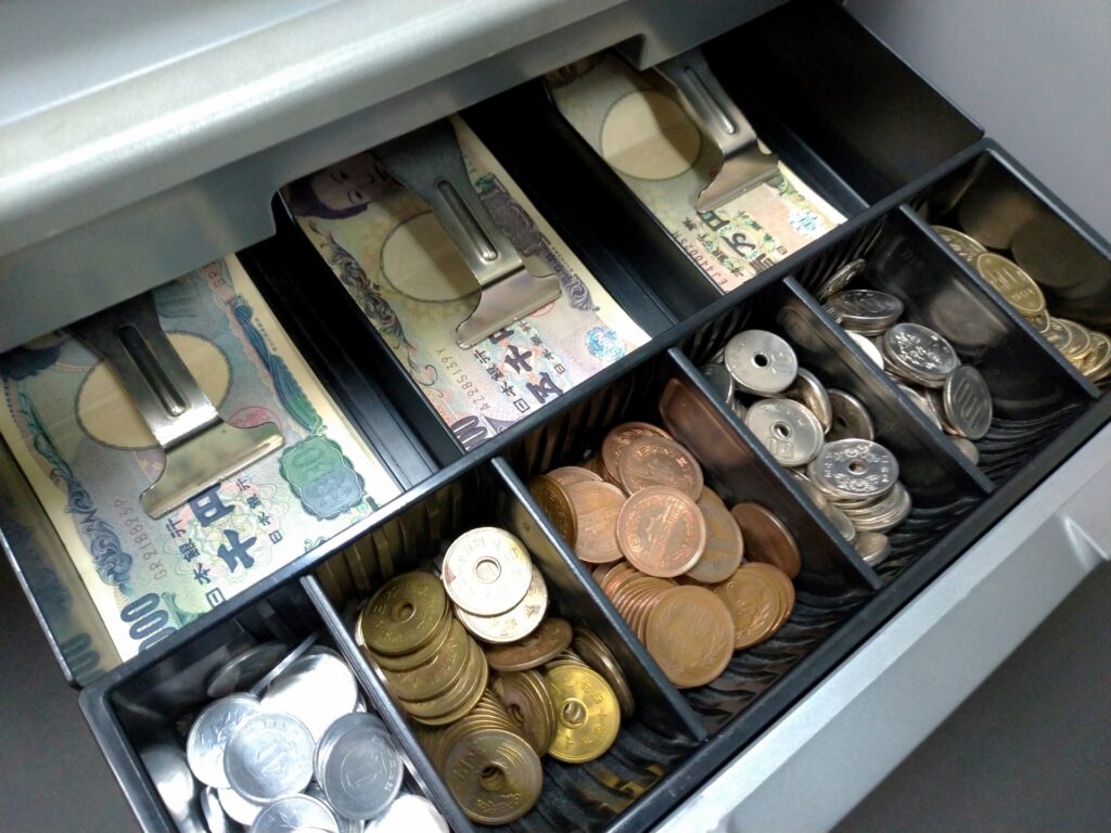 レジドロア内に種類ごとに整理された紙幣と硬貨。現金管理の基本である整理整頓を徹底し、会計時のミスや違算金を最小限に抑えます。店長に必要なマネジメント知識として、現場実務と評価を連動させ、利益漏れを防ぐための効率的なレジ運営の風景。