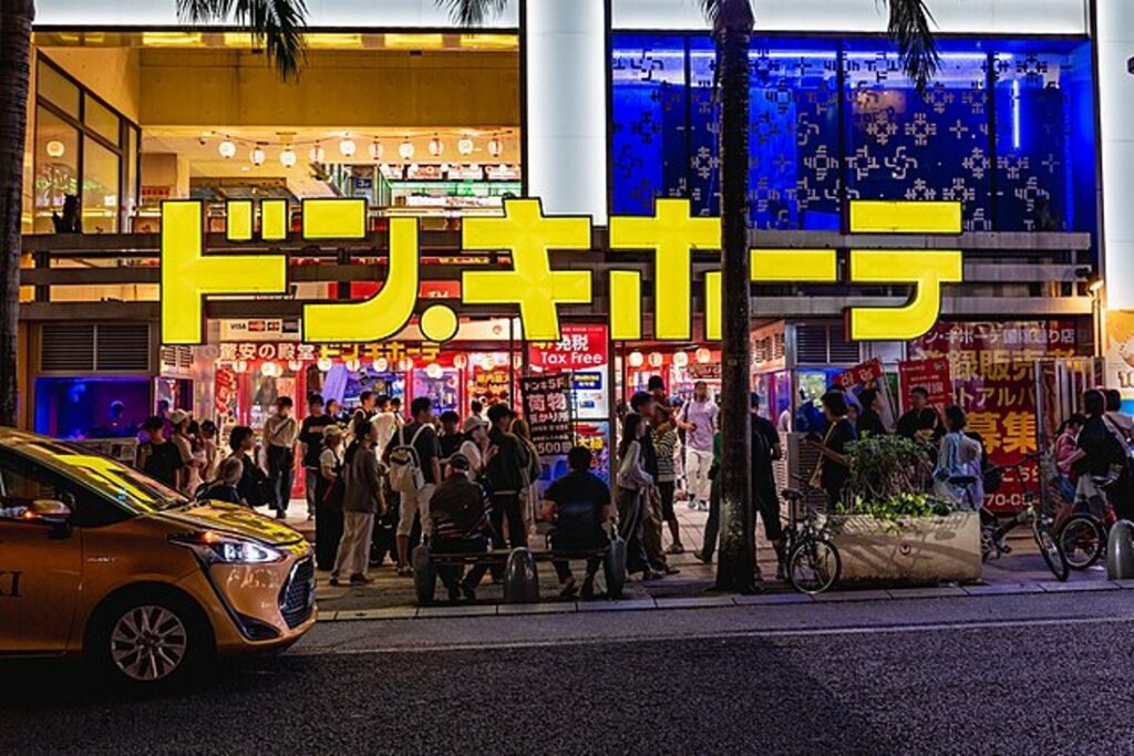 ドン・キホーテ国際通り店の夜景。中内功や柳井正が説いた「客層の創造」を具現化し、焼き芋を年間15億円のヒット商品へと育て上げた現場。ターゲットキーワードの「焼き芋販売戦略」と「店舗経営」を象徴する、24時間賑わう革新的な小売店舗の外観。
