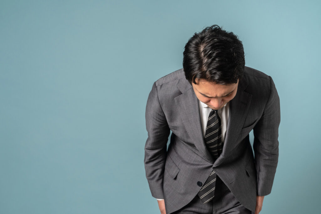 深々と頭を下げて謝罪するスーツ姿の男性。クレーム対応の要である誠実な姿勢を示し、失った信頼を回復させるプロセスを表現。店長マニュアルに基づく適切な苦情対応ノウハウで、リスクをチャンスに変え、固定客を育むためのプロのマネジメントイメージ。