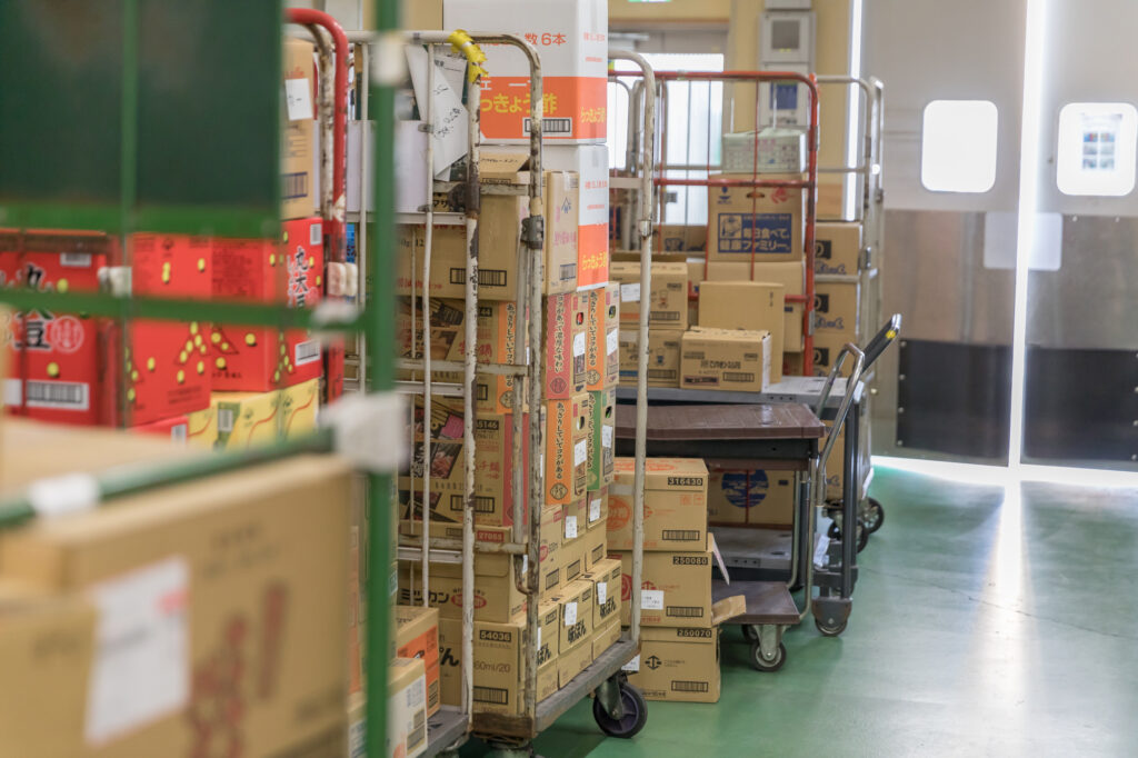 カゴ車と段ボールが整理された店舗のバックヤード。商品管理の要である荷受けと保管を標準化し、人件費削減と作業効率化を実現。理念・実務・評価を連動させた前向きなサイクルにより、パート・アルバイトと共に利益を育む、整理された現場の風景。