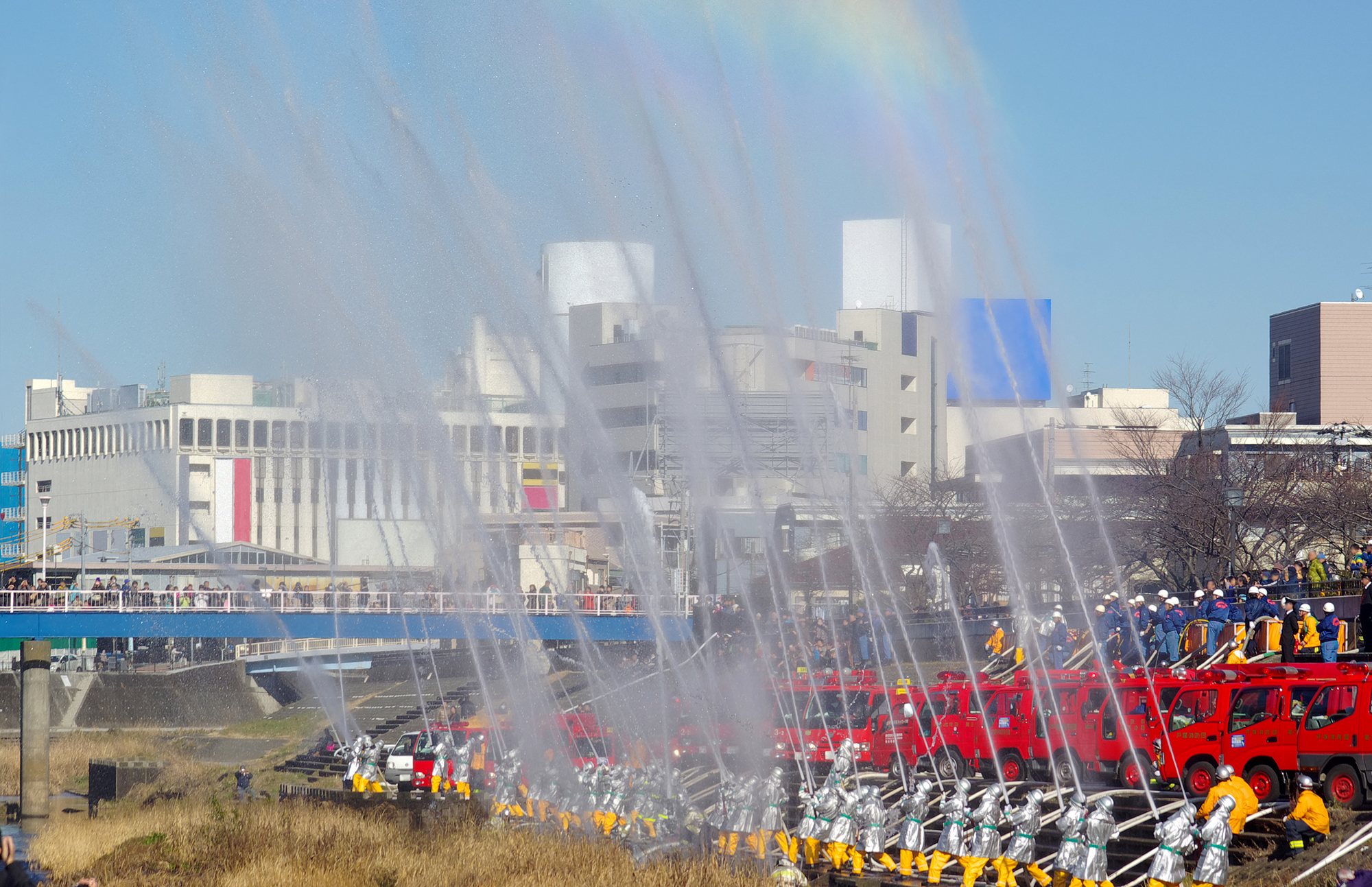 店舗の火災予防と防災意識を高める消防出初式の一斉放水風景。2026年の新年に店舗経営者が取り組むべき防火対策とBCP（事業継続計画）の重要性を象徴。地域の安全を守る消防団の活動を通じ、災害に強い店舗づくりとリスク管理の第一歩を想起させます