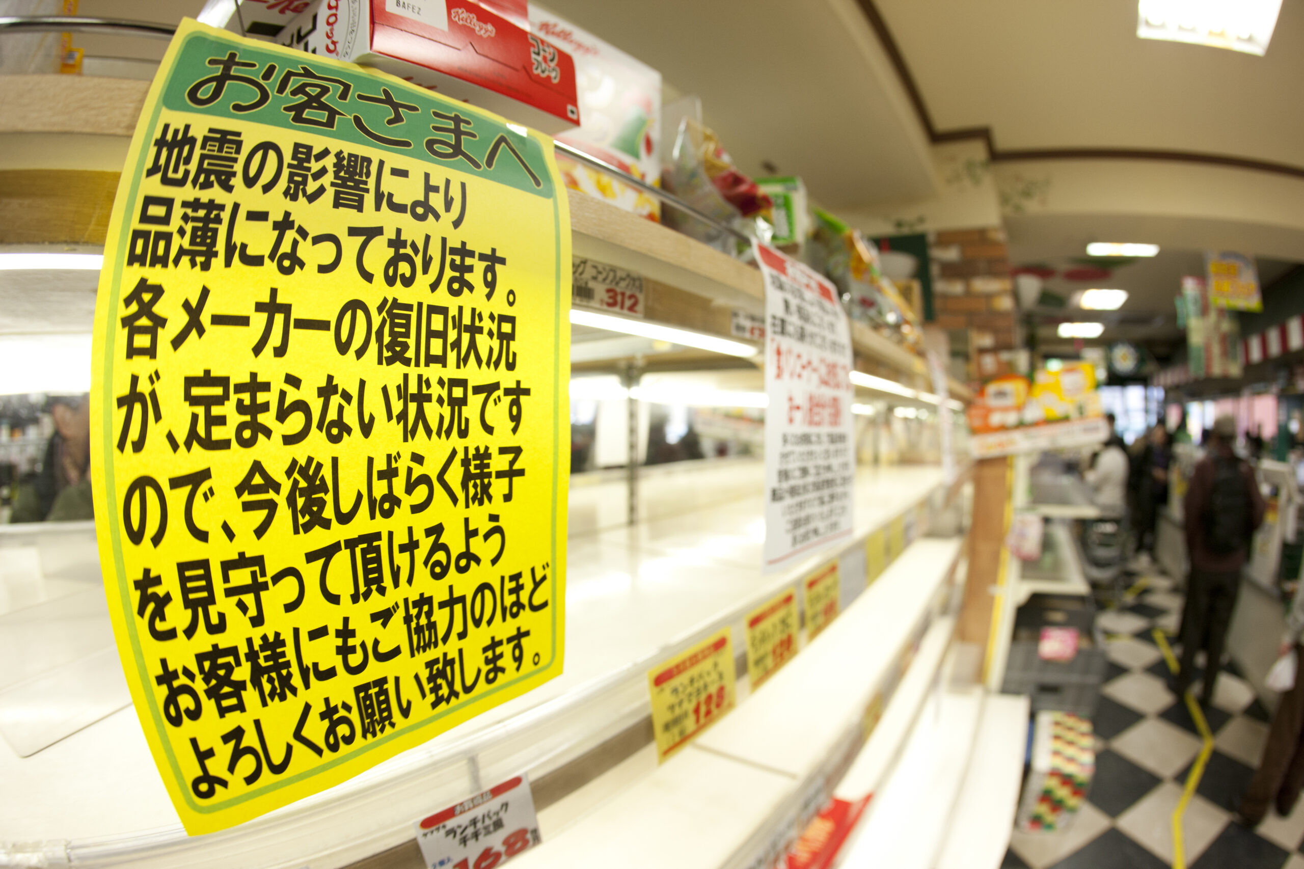 東日本大震災直後の品薄となった店舗の棚。災害時の供給網断絶や物流停滞のリスクを象徴し、店舗が自律的に営業を継続するために最低3日分以上の食料・水・備蓄品を自前で確保しておく必要性を客観的事実として伝えています。