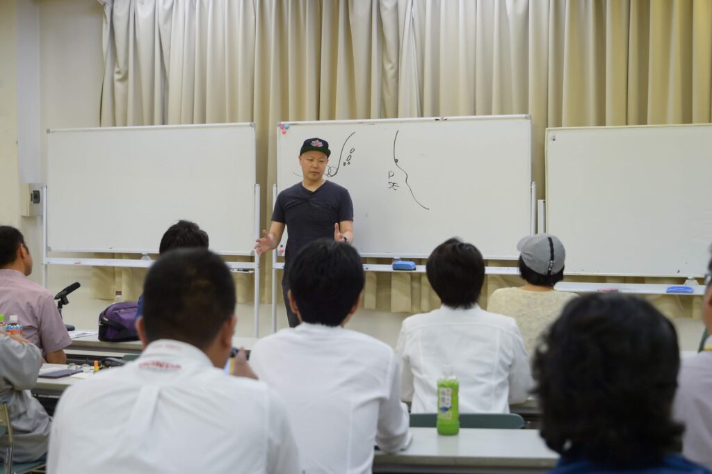 受講生を前に図解を交え講義する佐藤勝人氏。飲食・小売業の経営課題を解決するリーダーシップ教育と、採用・定着率を劇的に改善する目的思考のマネジメント手法を伝える研修会。店長不在でも稼げる店舗運営の秘訣を公開する場面。