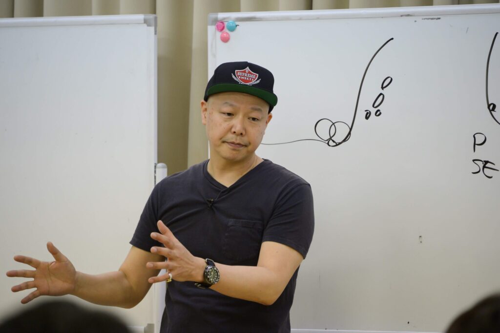 ホワイトボードの前で熱弁を振るう佐藤勝人氏。店舗経営者へリーダーシップの本質と人手不足を解決する仕組み作り、スタッフが自ら考えて動く組織への視点転換を直接指導するセミナー風景。専門性と信頼性を象徴する実践的教育の様子。