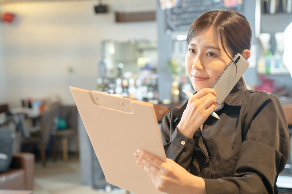 オートリザーブのAI予約電話に対応する飲食店の現場スタッフ。迷惑電話によるオペレーションの混乱を防ぎ、スタッフのストレス軽減と店舗運営の安定化を目指す。現場での電話対応ルールの徹底やスタッフ教育の重要性を象徴するプロフェッショナルな画像。