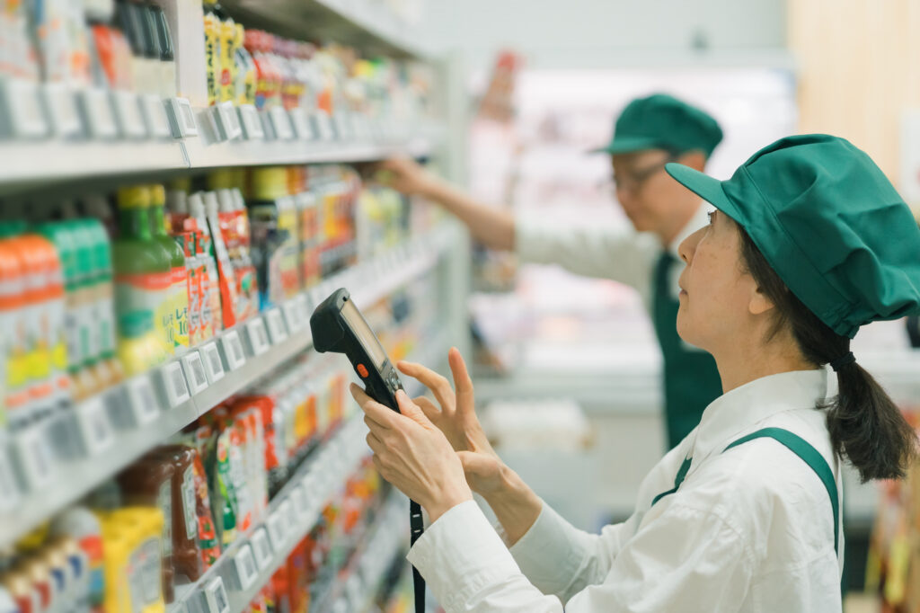 スーパーマーケットでハンディターミナルを使用して棚卸ロス(在庫管理)を行う店員の様子。適切な店舗運営と、不正を防ぐ業務標準化・POS管理のイメージ。