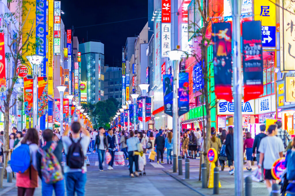 夜の池袋サンシャイン60通りの繁盛立地風景。多くのチェーン店が立ち並ぶエリアは、人流調査や商圏分析における店舗出店戦略の重要なモデルです。視認性と集客力の高い一等地の特徴を把握するためのイメージ画像。