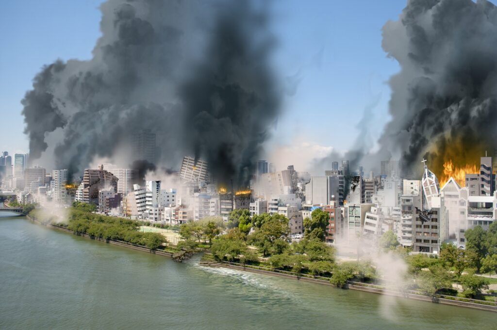 大規模な地震や火災により煙が上がる市街地と店舗被害のイメージ。POSレジやPC機器全滅時でも営業再開を可能にするため、顧客データや売上情報をクラウドへ二重保全する情報BCPの重要性。