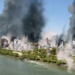 大規模な地震や火災により煙が上がる市街地と店舗被害のイメージ。POSレジやPC機器全滅時でも営業再開を可能にするため、顧客データや売上情報をクラウドへ二重保全する情報BCPの重要性。