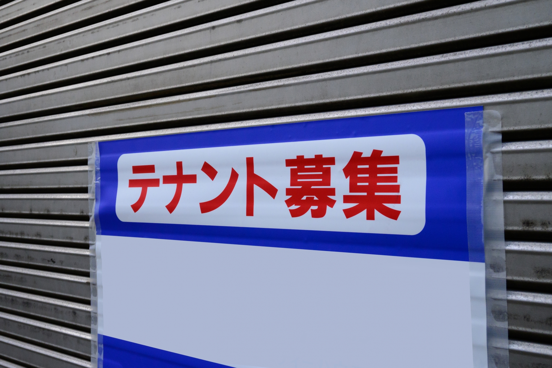 「テナント募集」の看板が掲げられた物件のシャッター。コンビニ跡地などの居抜き物件は、戦略的な立地評価と適正な家賃交渉を行うことで、中小店舗経営者がコストを抑えながら利益を最大化する再構築の機会となります。