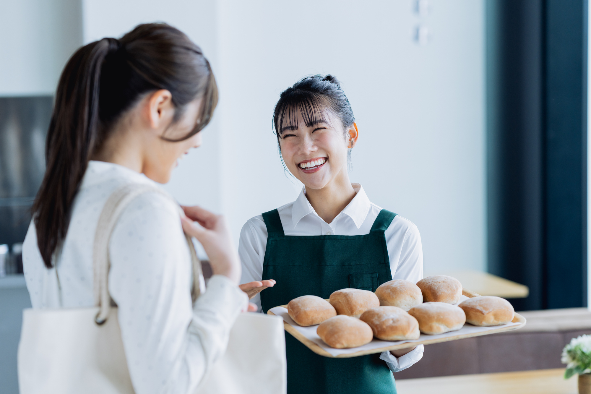 飲食・小売店の店頭で笑顔でお客様へ推奨販売を行うスタッフ。押し売り感を排除し、顧客満足度（QSC&V）を高めながらアルバイトでも無理なく客単価と買上点数を伸ばすサジェスト運用の実践風景。