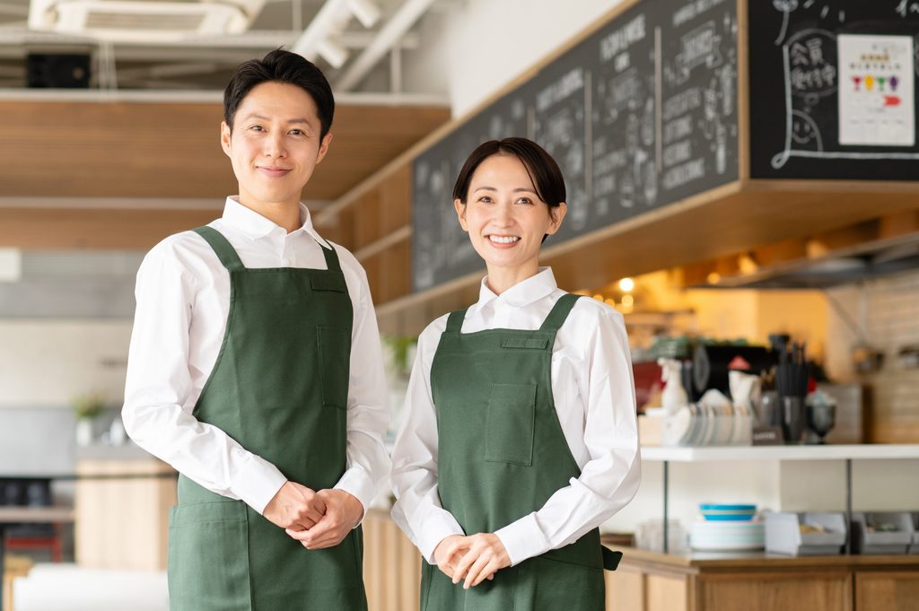 エプロンを身につけ笑顔で接客に臨む店舗スタッフ。真のお客様第一とはスタッフの過酷な自己犠牲ではなく、早期予約の仕組みによって労働環境を整え、高い顧客満足と適正利益を無理なく両立させる経営の実践にある。