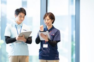 介護士　女性トレーナー　仕事を教わりマニュアルにメモをする新人男性