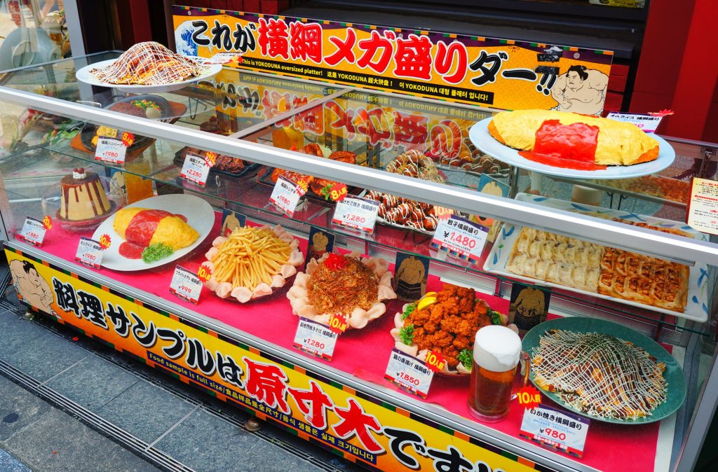 ギルティ飯、背徳飯、増量で消費者の心と胃袋を掴む差別化戦略で売上アップ！串カツ横綱の「名物MEGA盛り」。焼きそば、オムライスなどのメニューで、最大、通常の20倍のボリュームで原寸大の食品サンプルとPOPでの訴求は通行人を惹きつける
